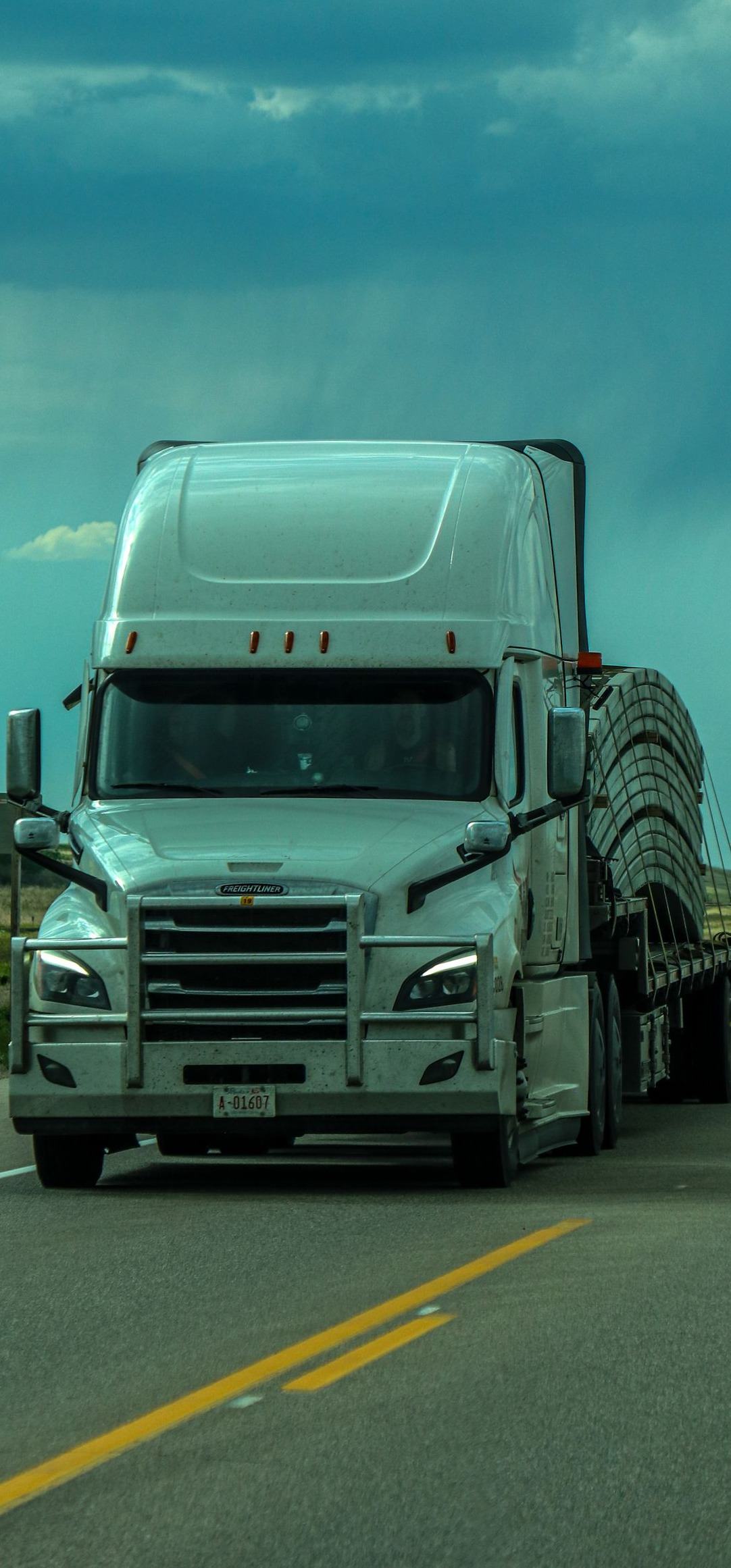 A white tractor unit head on with its trailer behind it on an open interstate
