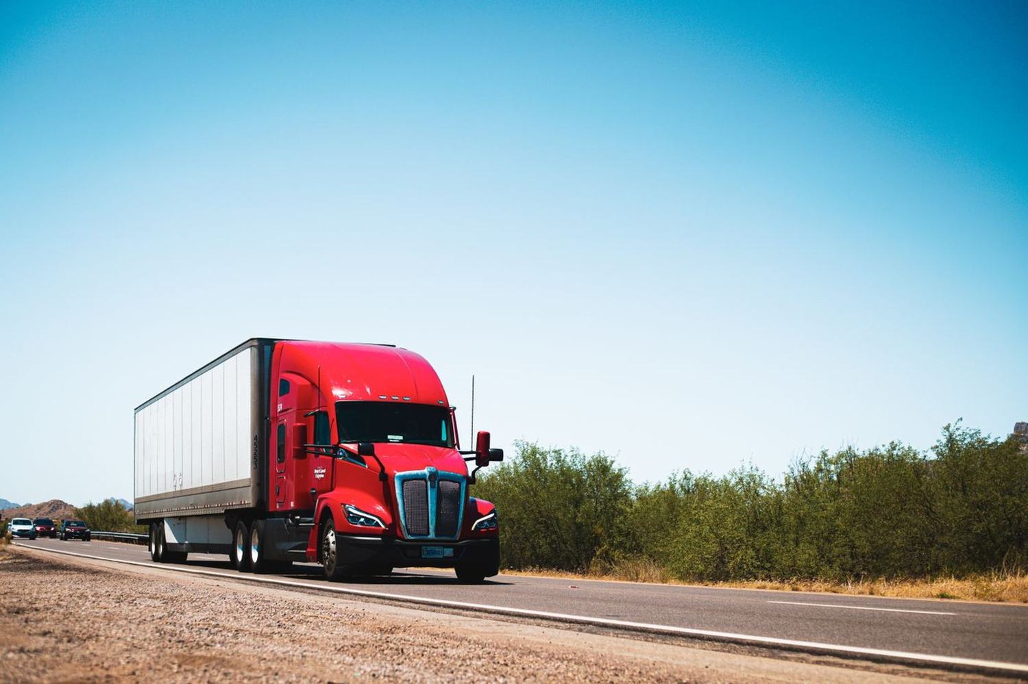 A red semi truck pulling a dry van trailer on a Texas interstate